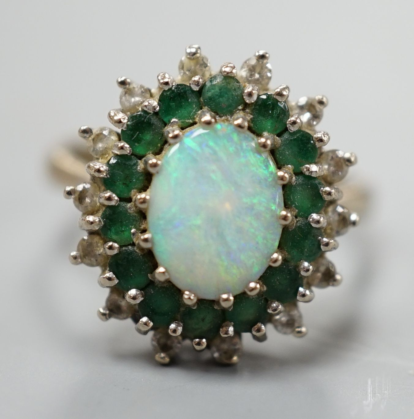 An 18ct white metal, white opal, emerald and diamond set oval cluster ring, size O, gross weight 6.2 grams.